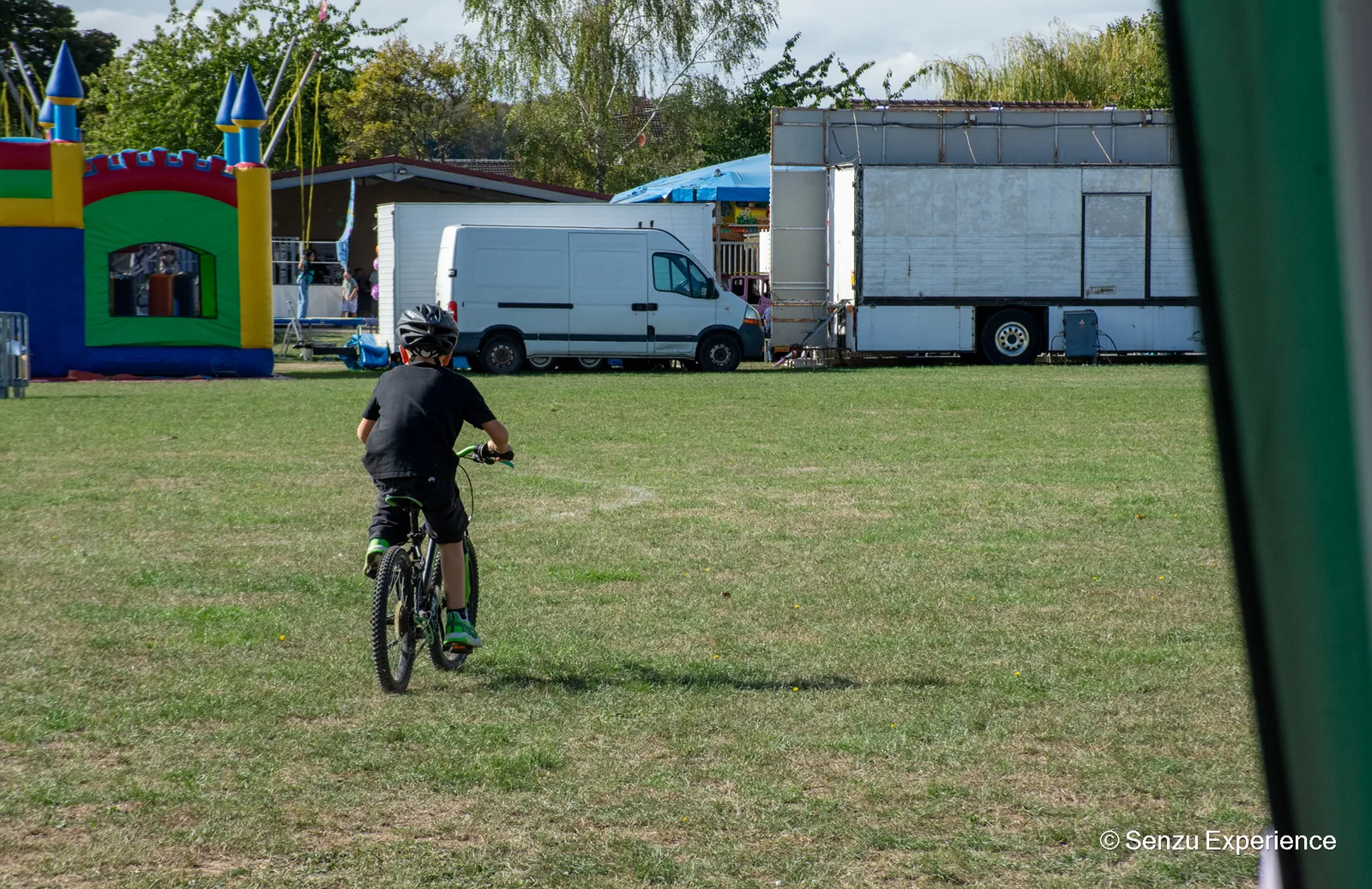 Un enfant roule sur le stade, la f&ecirc;te foraine de Villeneuve-les-Sablons install&eacute;e en arri&egrave;re-plan